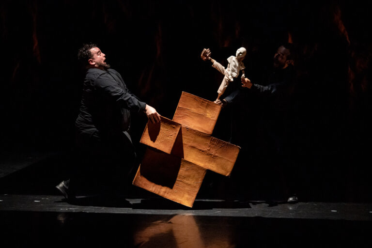 Photo du spectacle : un homme bascule le promontoire de cartons sur lequel danse la marionnette